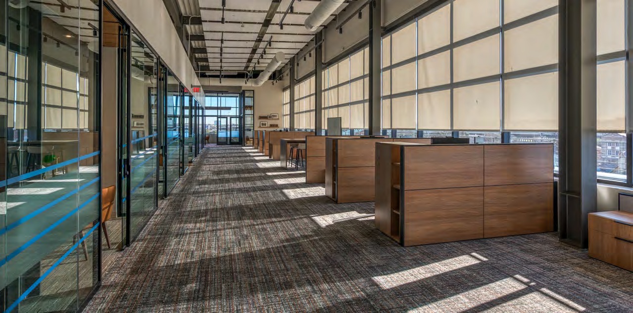 An open Light Building workspace with collaborative desks, exposed ceilings, and tall windows.